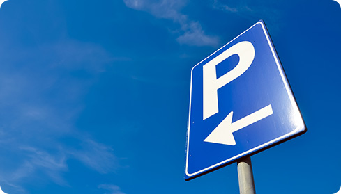 Image: a blue directional "P" sign pointing to a car park on a sky background